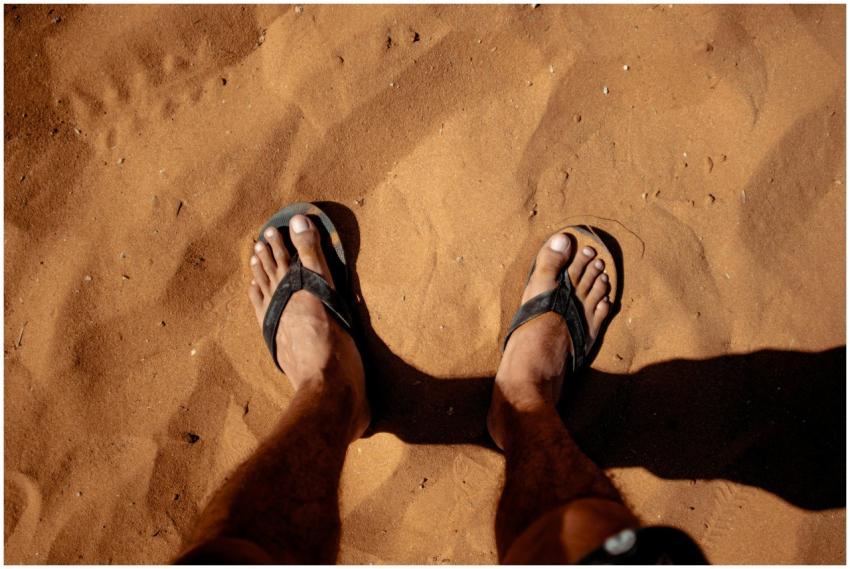 Close-up of feet in flip flops standing on sunlit