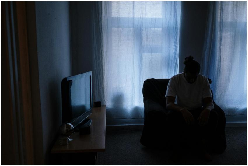 A person sits alone in a dimly lit room, reflectin