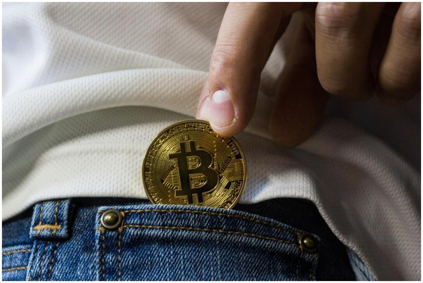 Close-up of hand putting Bitcoin in jeans pocket s