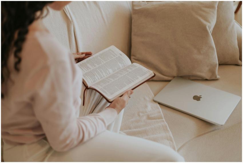 Woman reading a book on a cozy sofa with a laptop