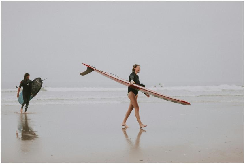 A woman carrying a surfboard on the sandy shore of