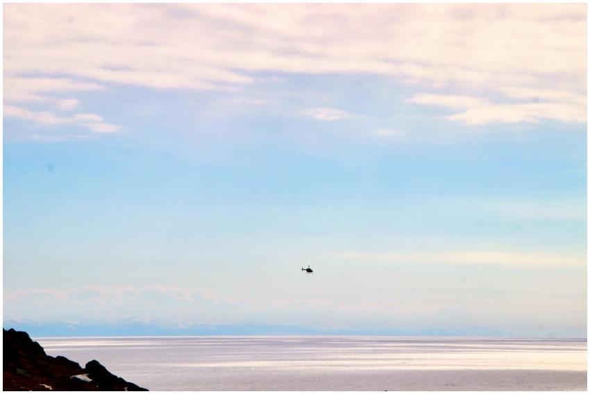A helicopter flies above a calm ocean during a bea