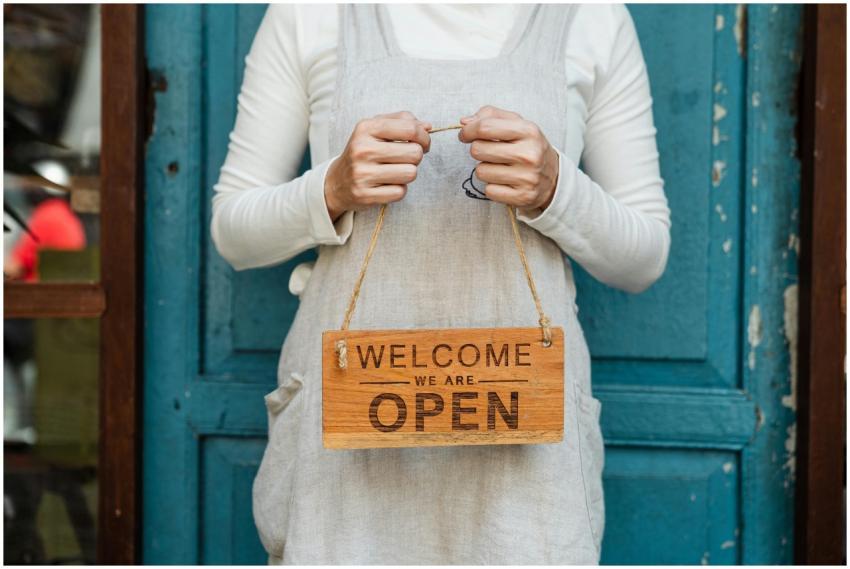 A person holds a "Welcome, we are open" sign in fr