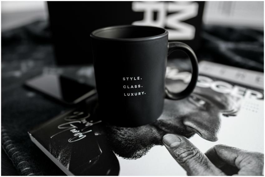 A stylish black mug with text sits on a luxury mag