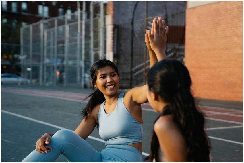 Two women in activewear high-fiving on a city stre