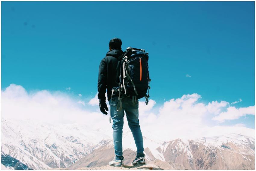 A lone hiker with a backpack surveys snow-capped m