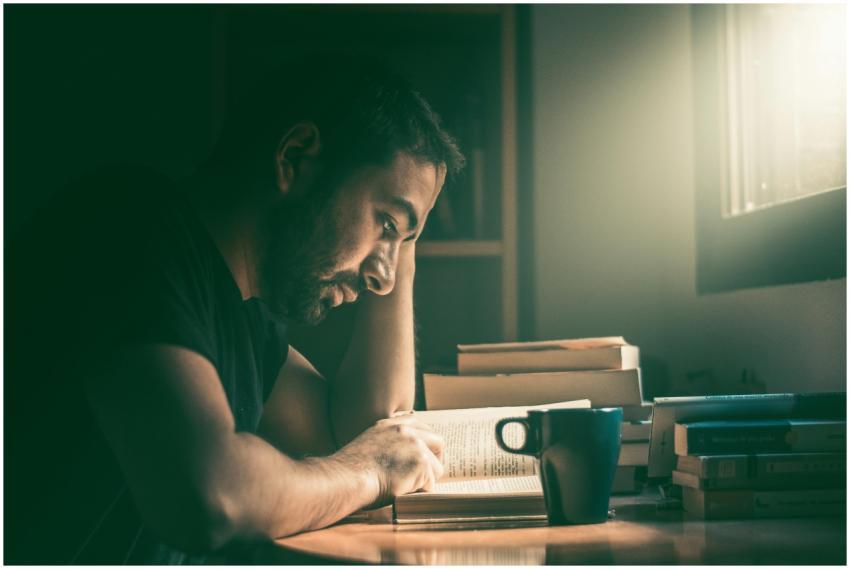 An adult man immersed in reading by the window in