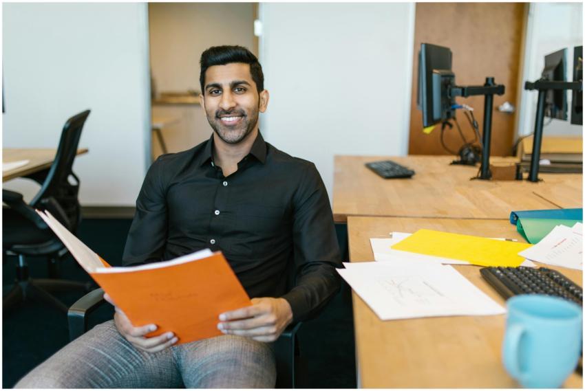 Smiling businessman holding documents at his desk,