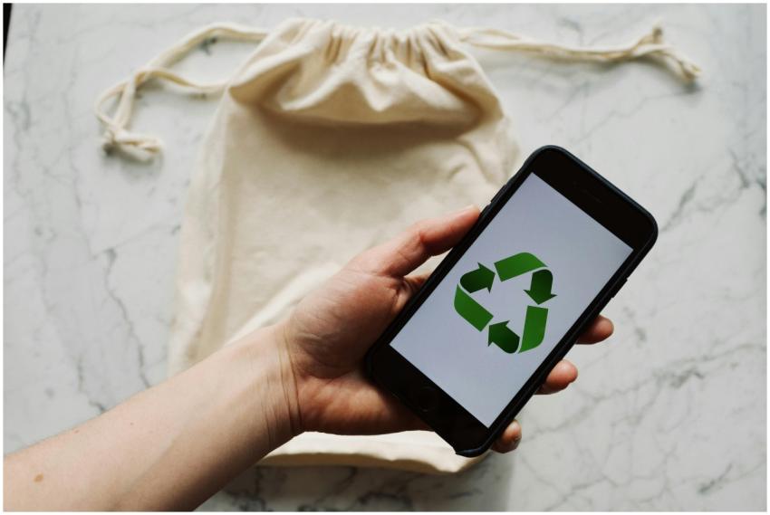 A hand holds a smartphone showing a recycling symb