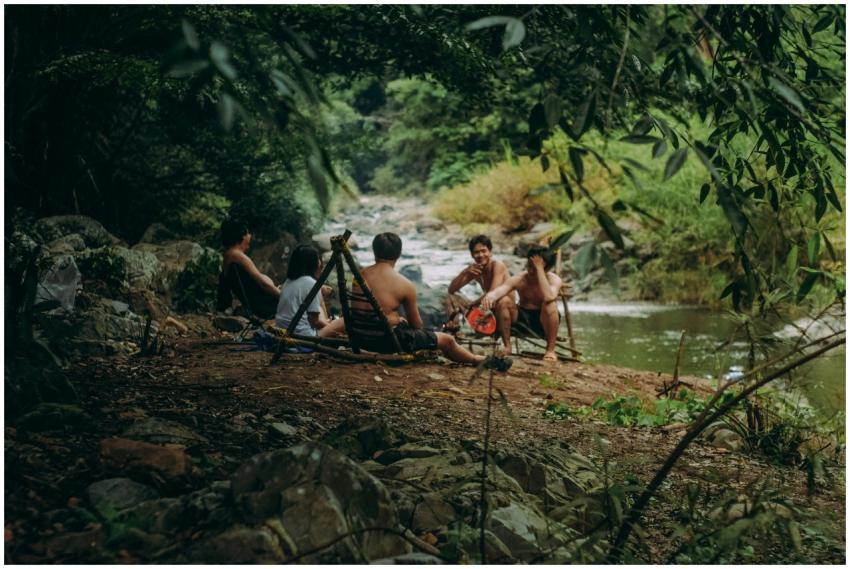 A group of adults relaxing and eating by a riverba