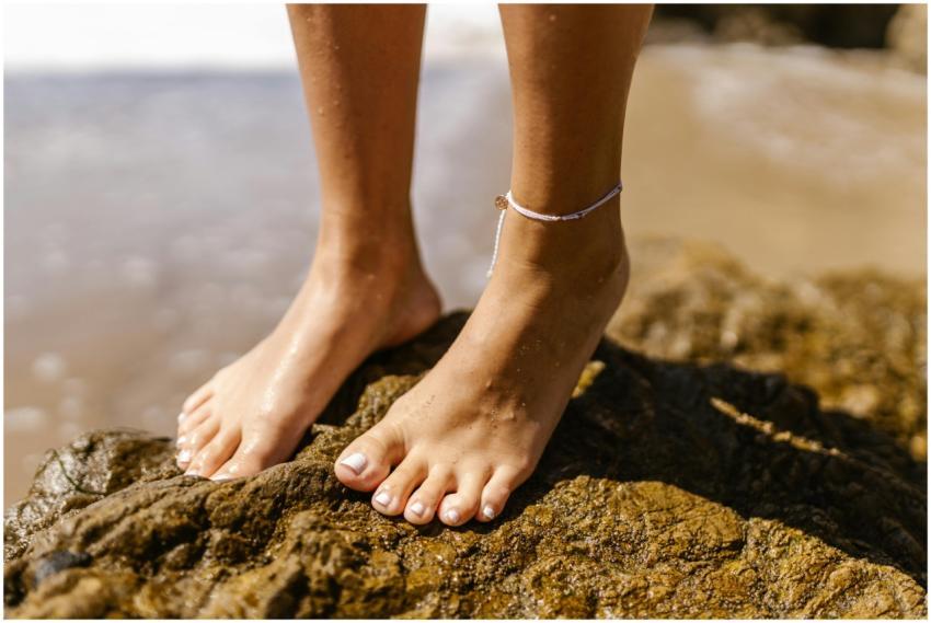 Close-up of bare feet and anklet on rocky shore, s