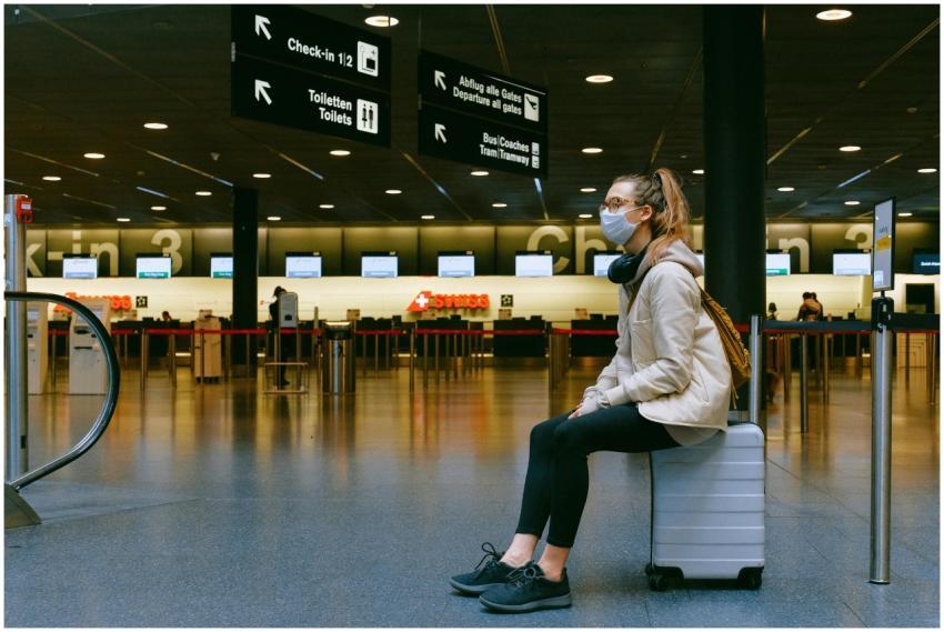 A woman wearing a face mask sits on luggage in an