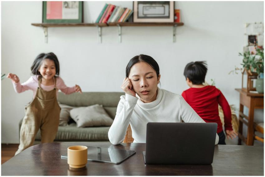 A tired mother working on a laptop while her child