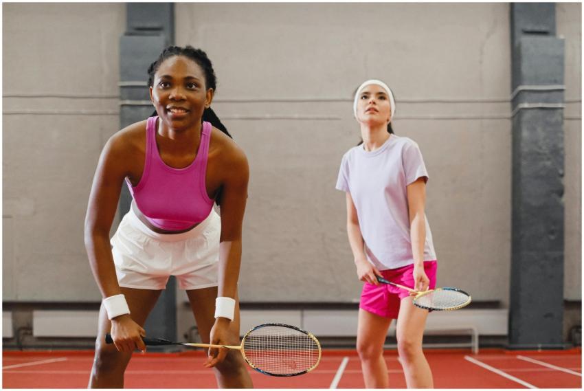 Two women playing badminton indoors, focusing on a