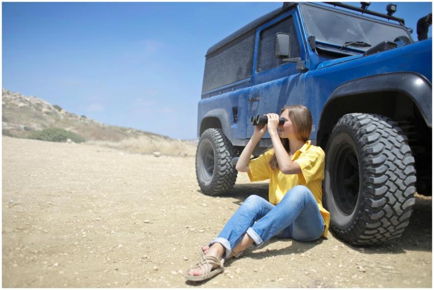 A woman sitting by a blue jeep in a desert landsca
