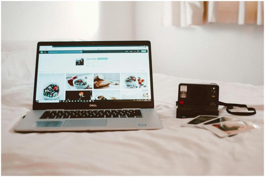A Dell laptop and vintage camera on a bed create a
