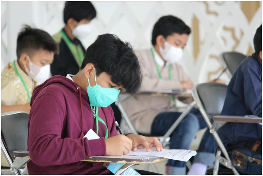 Teenagers wearing masks sit for an exam in an indo