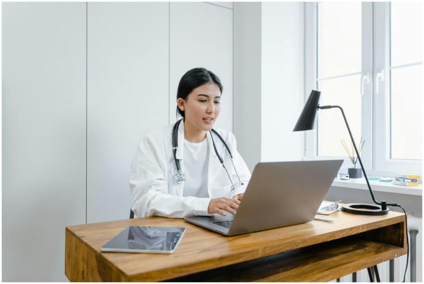 A female doctor in a white coat uses a laptop for