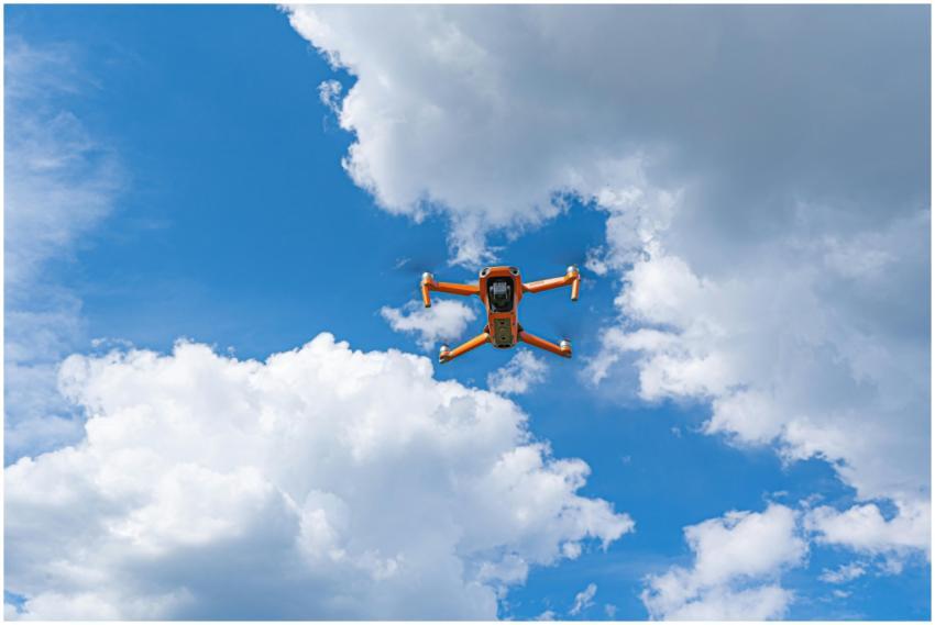 Orange drone flying against a dramatic cloudy sky,