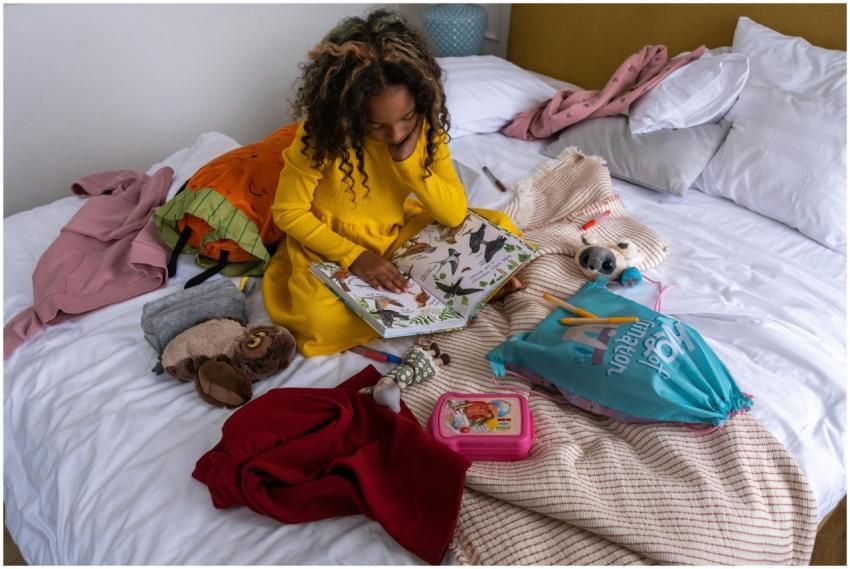 Young girl reading a book on a bed, surrounded by