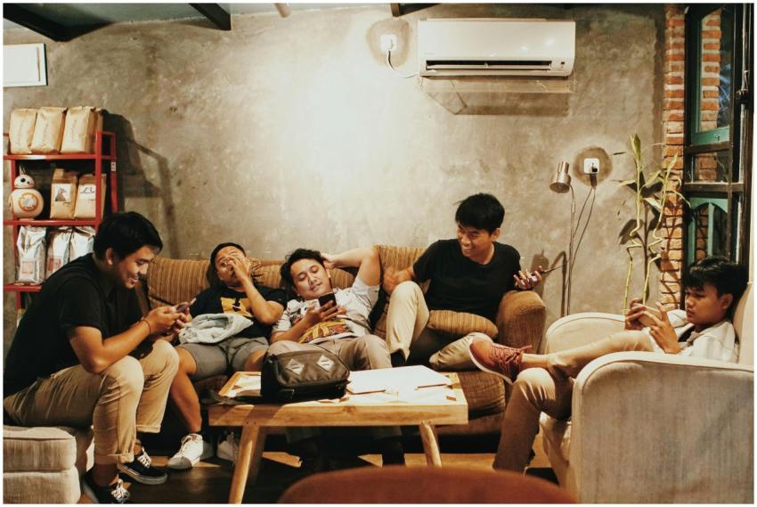 Five young men relaxing indoors, chatting and usin