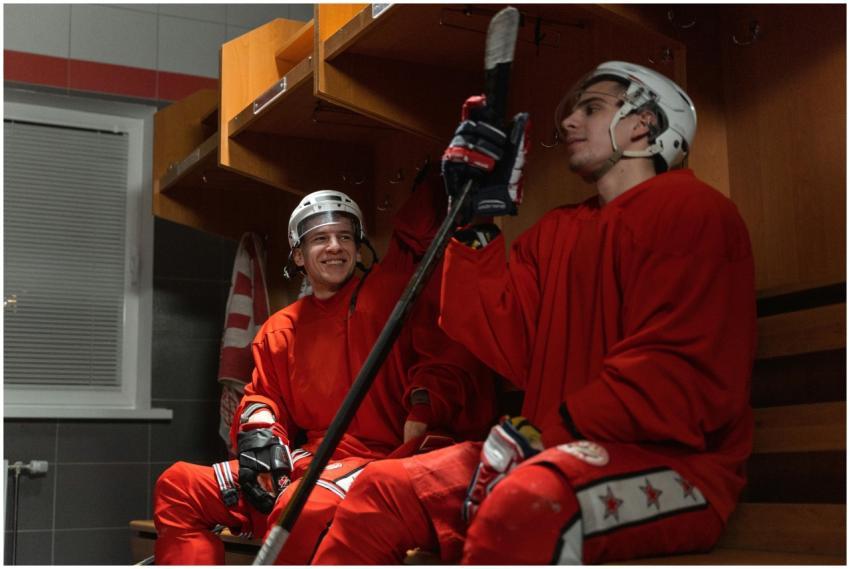 Two ice hockey players in locker room, sitting and