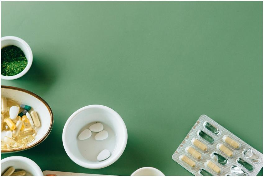 A flat lay of assorted pills and herbs on a green