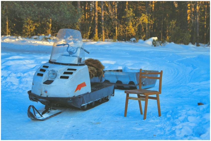 A snowmobile and wooden chair are set on a snowy p