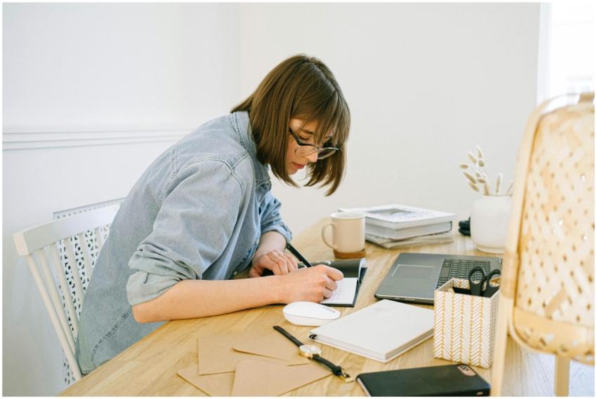 A young woman working from home, writing notes at