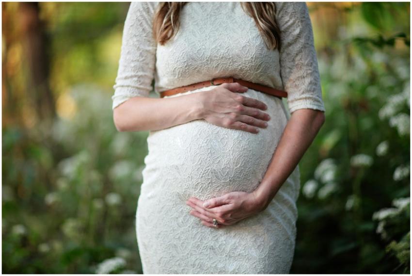 A pregnant woman in a lace dress gently cradling h