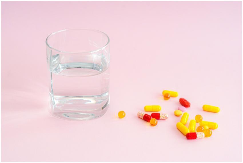 A glass of water and variety of pills on a pink ba