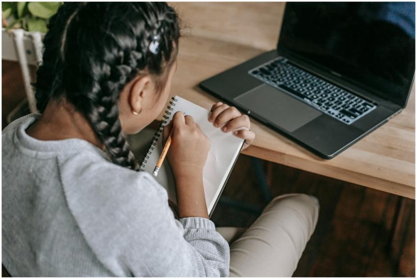 Young girl writing in a notebook with a laptop, sh