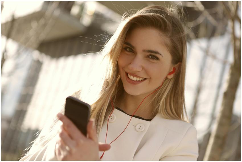 A smiling woman with headphones and smartphone enj