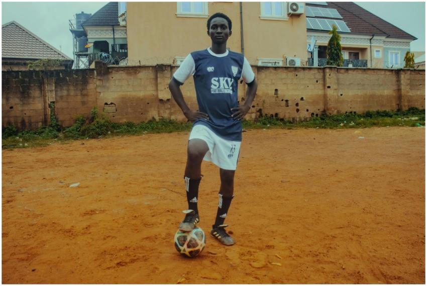 A teenage soccer player in uniform poses with a ba