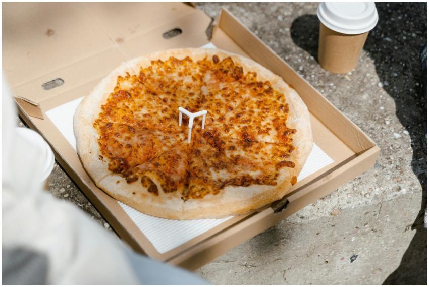 Cheesy pizza in an open box with a disposable cup,
