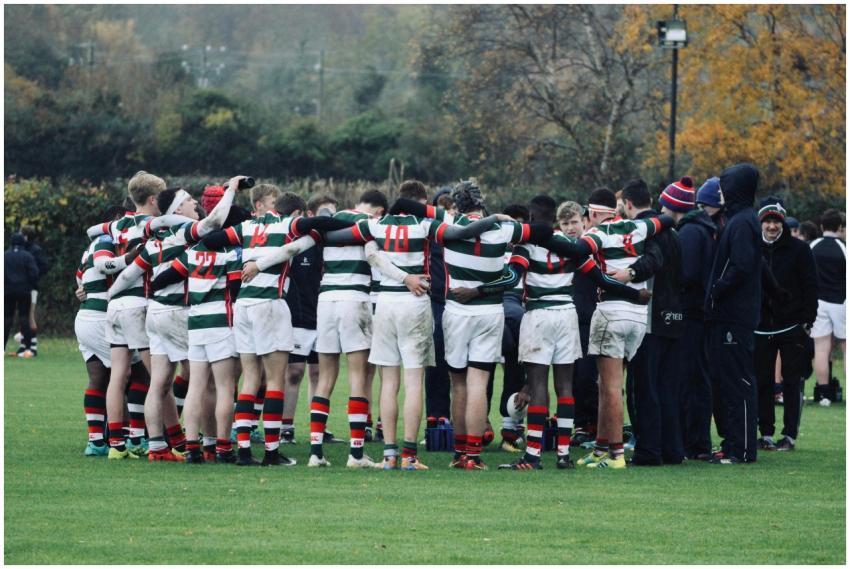 Rugby players in striped jerseys huddle during a g