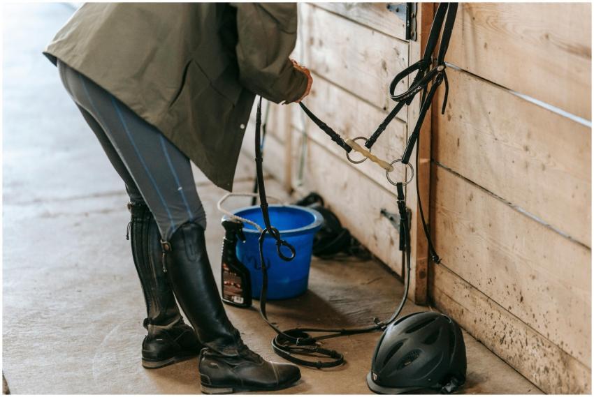 Person preparing horse tack in a stable, focusing