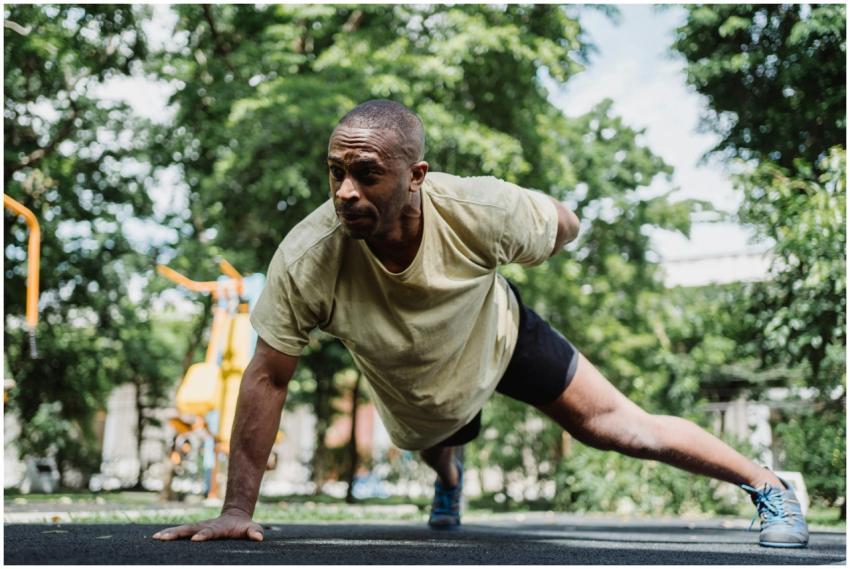 Man performing a one-arm push-up outside in a sunn