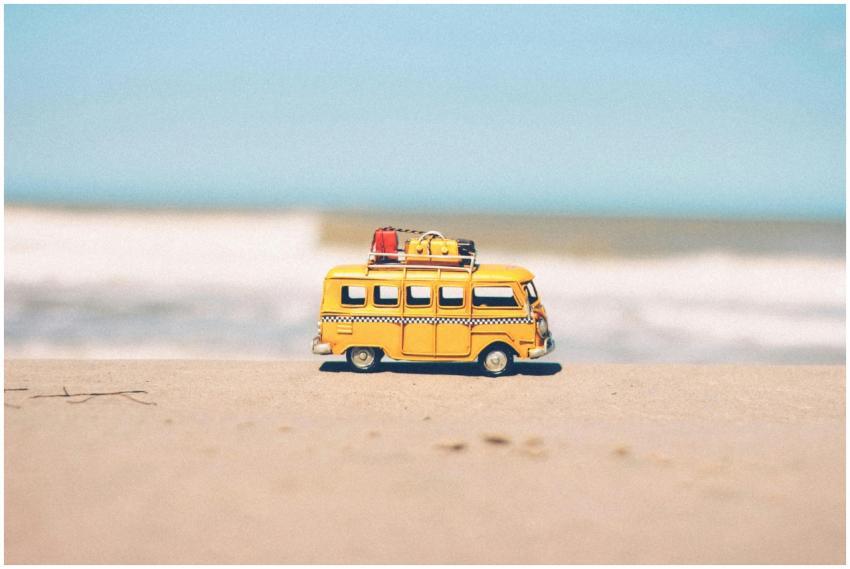 A vibrant yellow toy van sits on a sandy beach wit