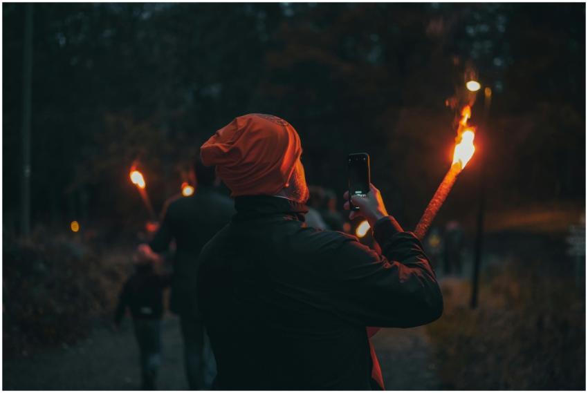 A person photographs a torch-lit walk at night usi