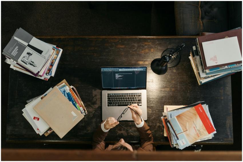 High-angle shot of a busy desk with books, laptop,
