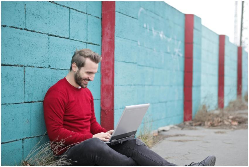 A man smiling and using a laptop outdoors against