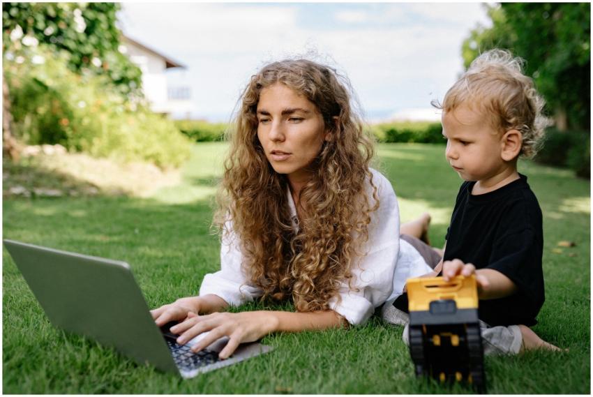 Woman working on a laptop while lying on grass wit