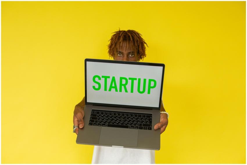 A young black man holds a laptop displaying 'Start