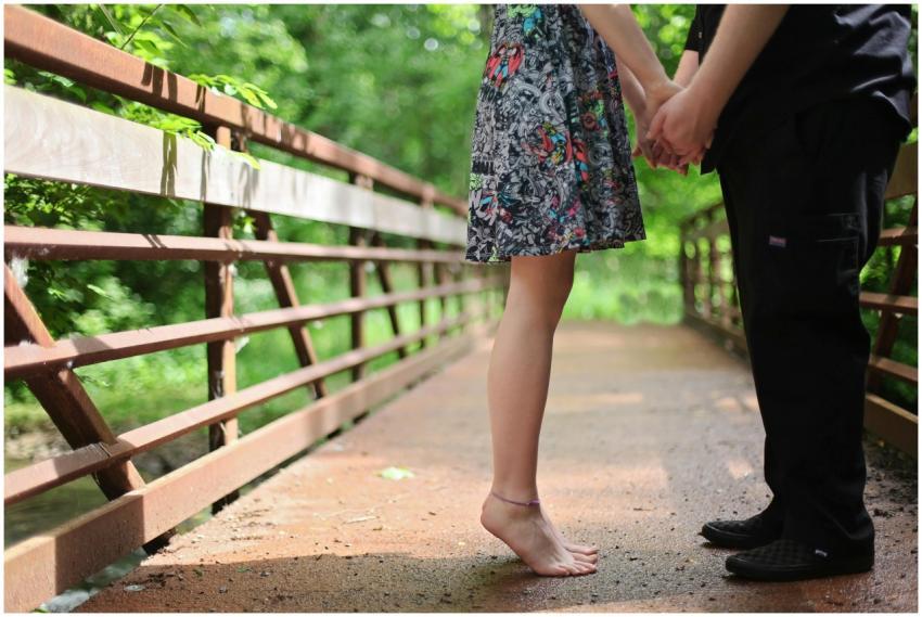 A barefoot couple holding hands on a wooden bridge