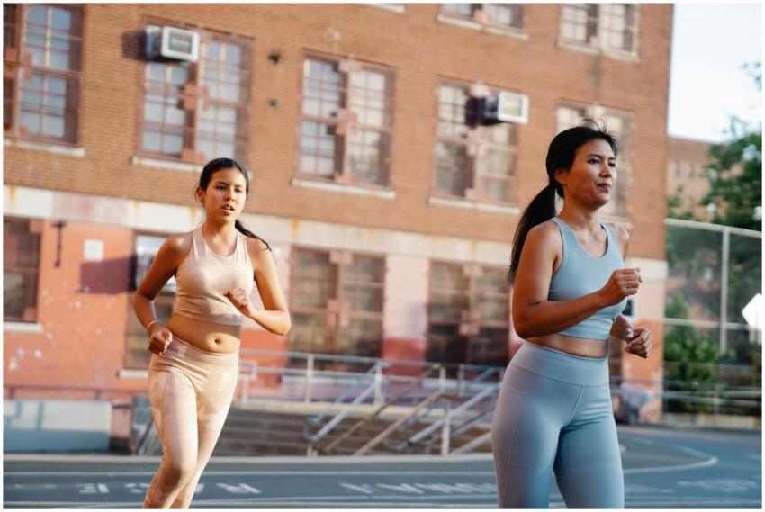 Two women jogging on an outdoor court near a brick