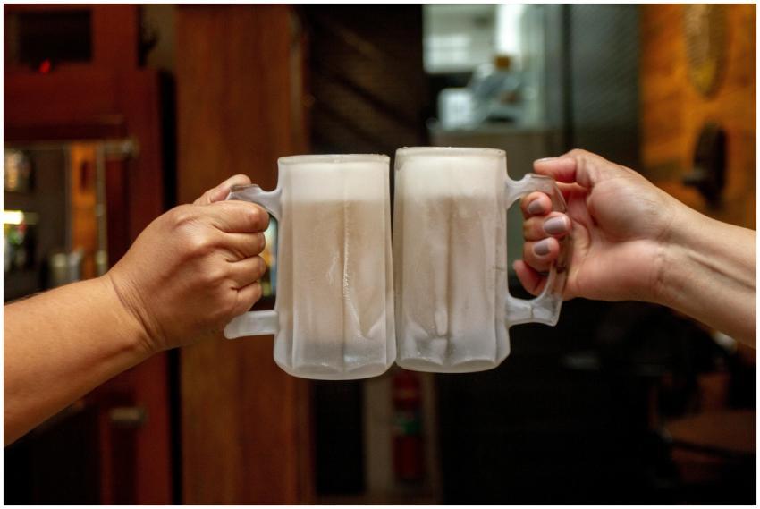 Two people clinking frosty beer mugs indoors, cele