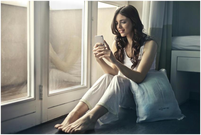 Young woman sitting by the window using smartphone