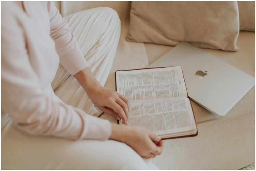 A woman in casual attire reads a book beside a lap