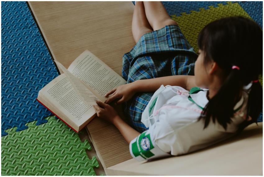 A young girl in a school uniform reading a book wh